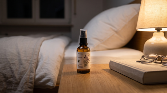 Kissenspray in der Braunglasflasche auf dem Nachttisch neben Buch und warmer Leselampe